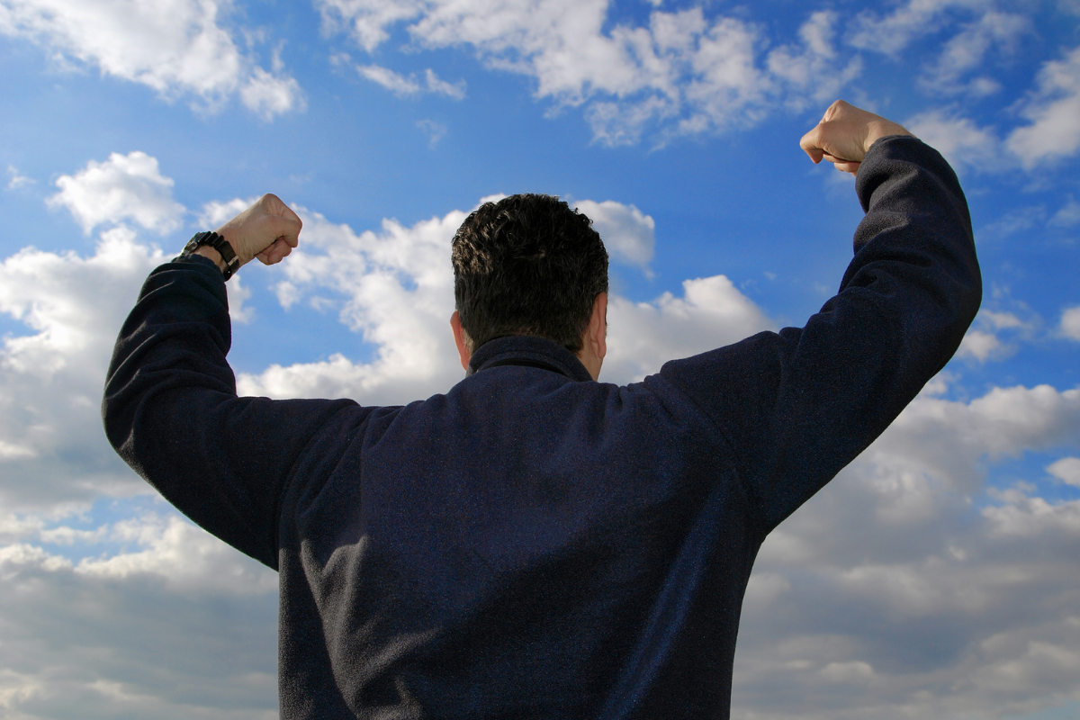 Man standing with arms raised in victory against a blue sky