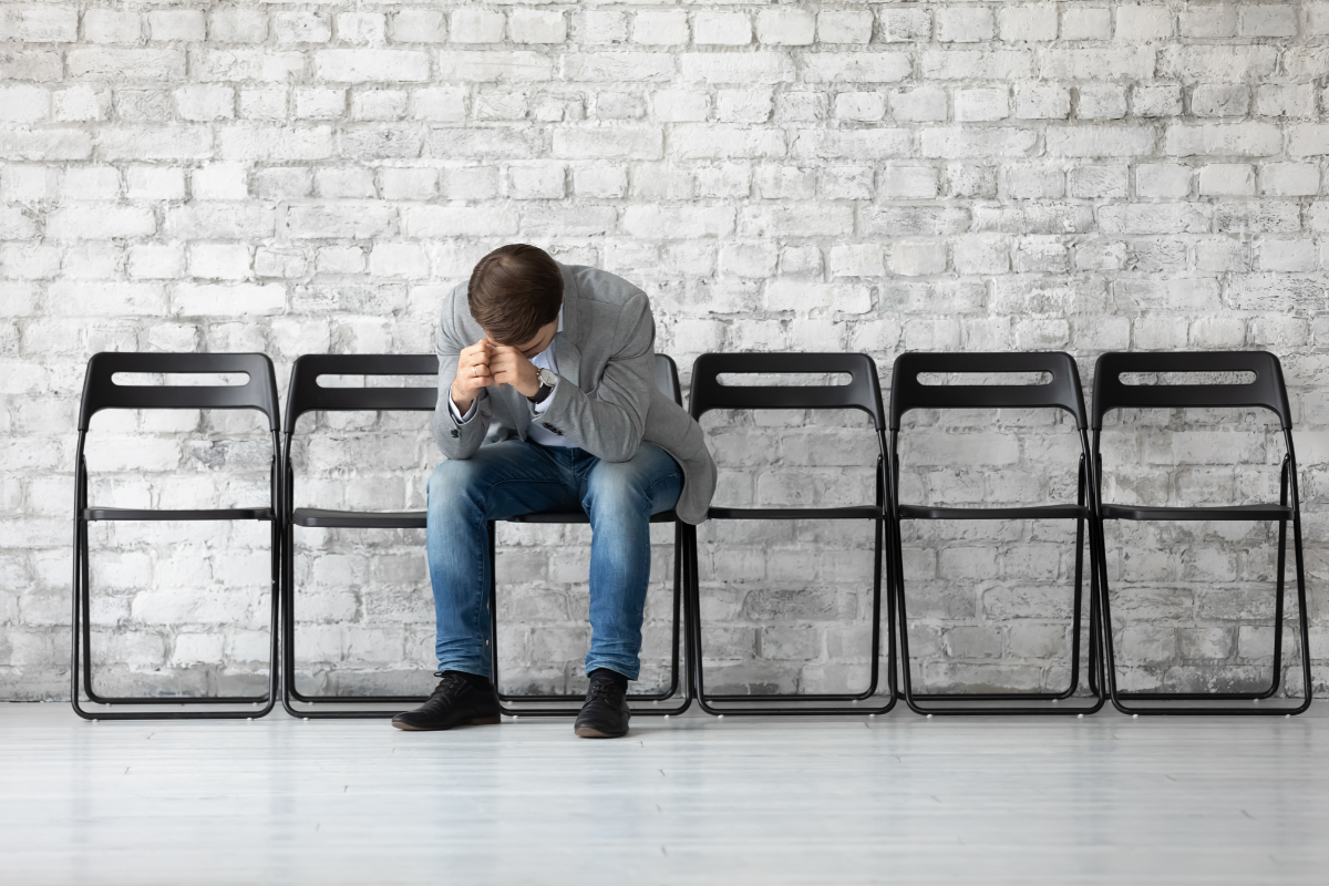 An image of a man bowing down his head in his hands while seated in a row of black chairs.