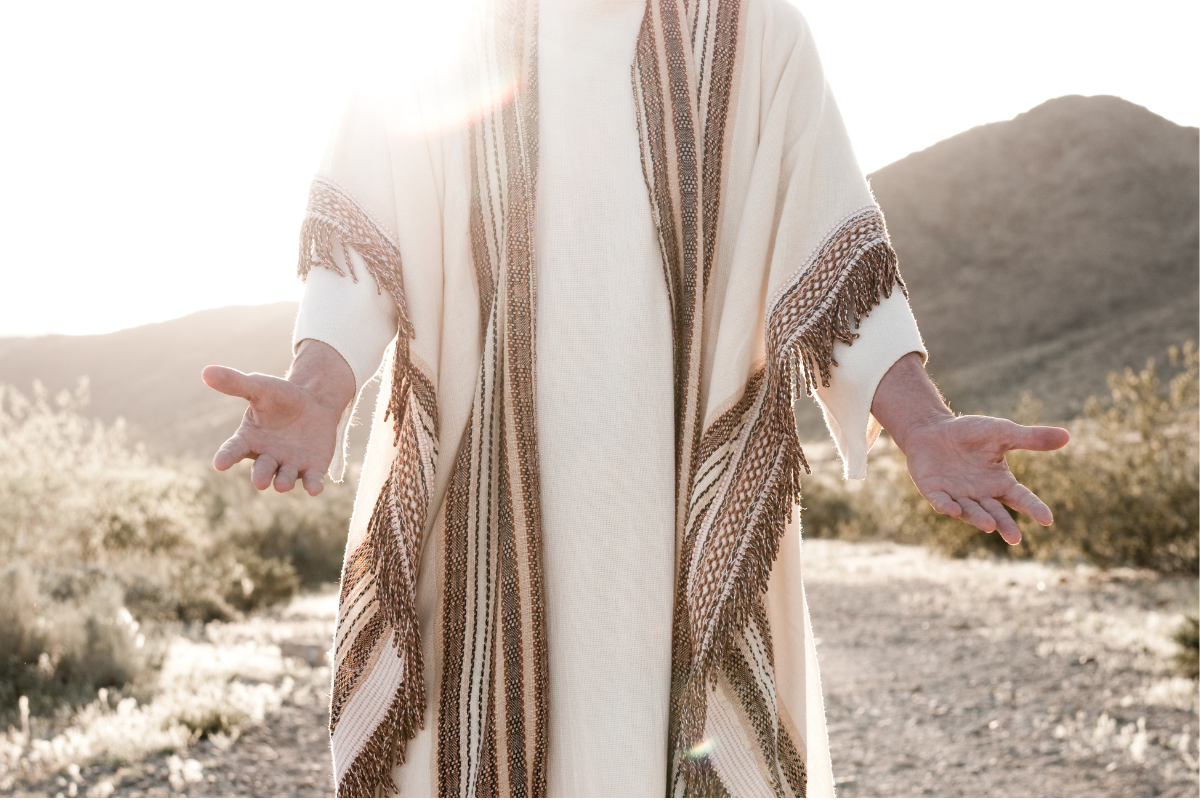 A figure resembling Jesus stands in a desert landscape with open, welcoming arms, symbolizing invitation, peace, and spiritual connection.