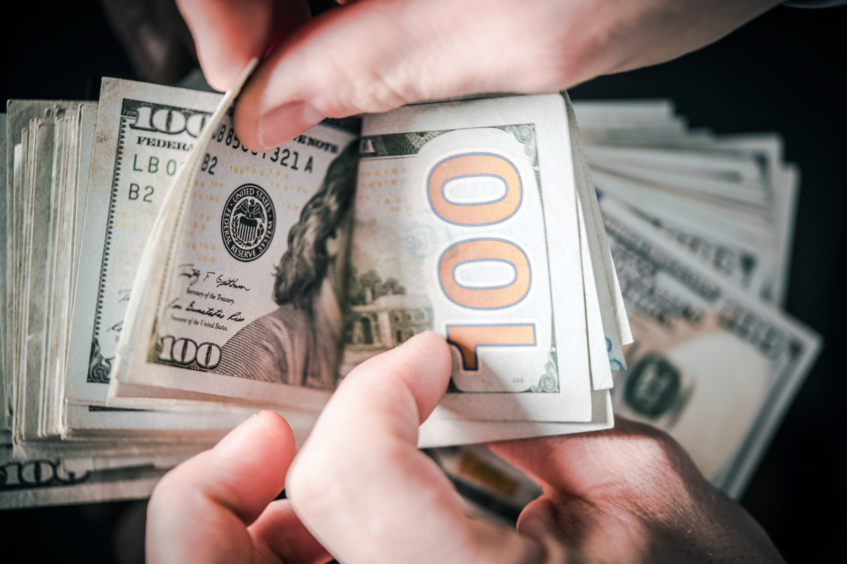 An image of hands counting 100-dollar bills.