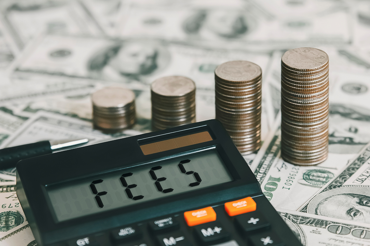 A calculator with the word FEES in it, surrounded by dollar bills and coins.