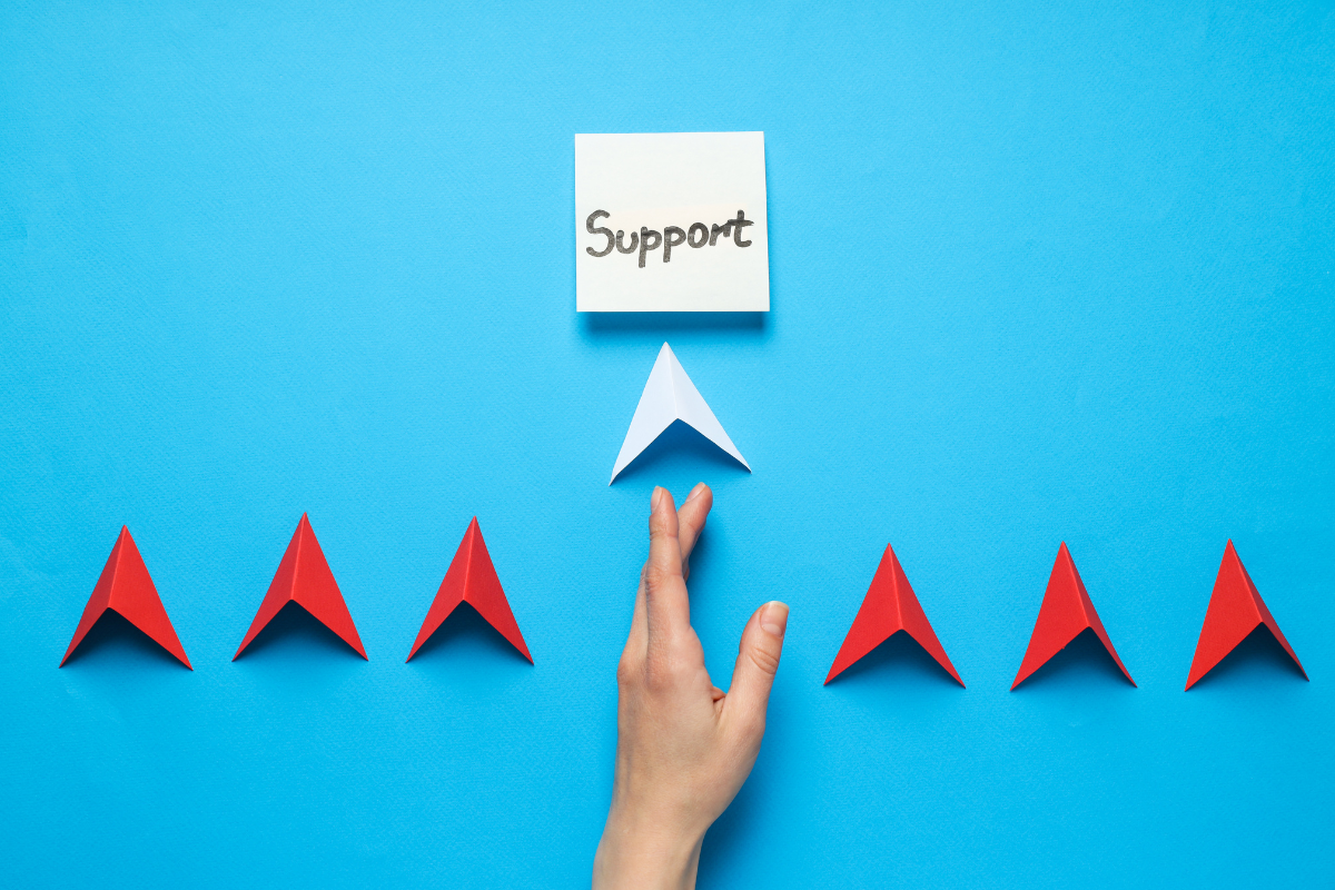 A hand guiding a white paper arrow toward a note labeled "Support," surrounded by red arrows on a bright blue background.