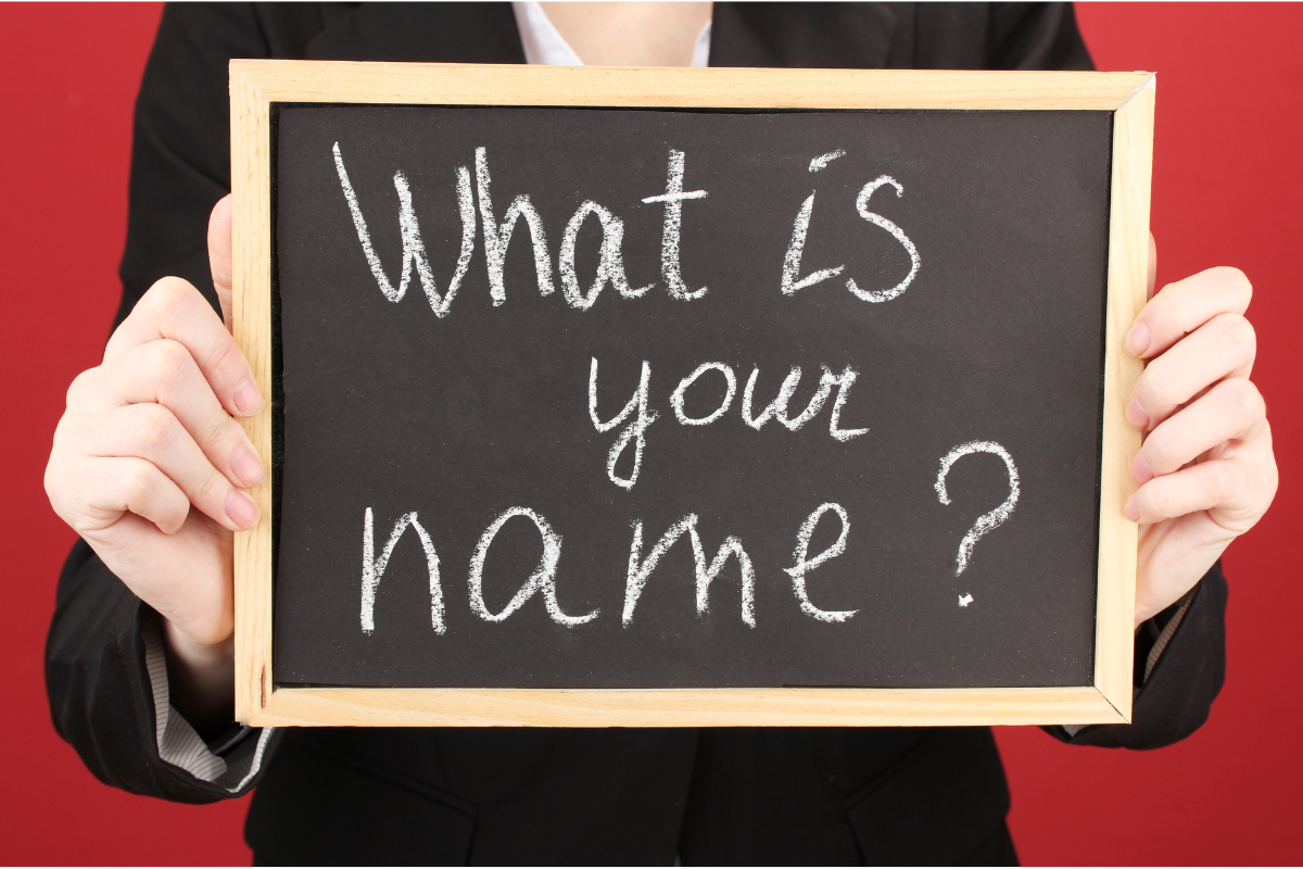 A person holding a chalkboard with the words "What is your name?" written on it.