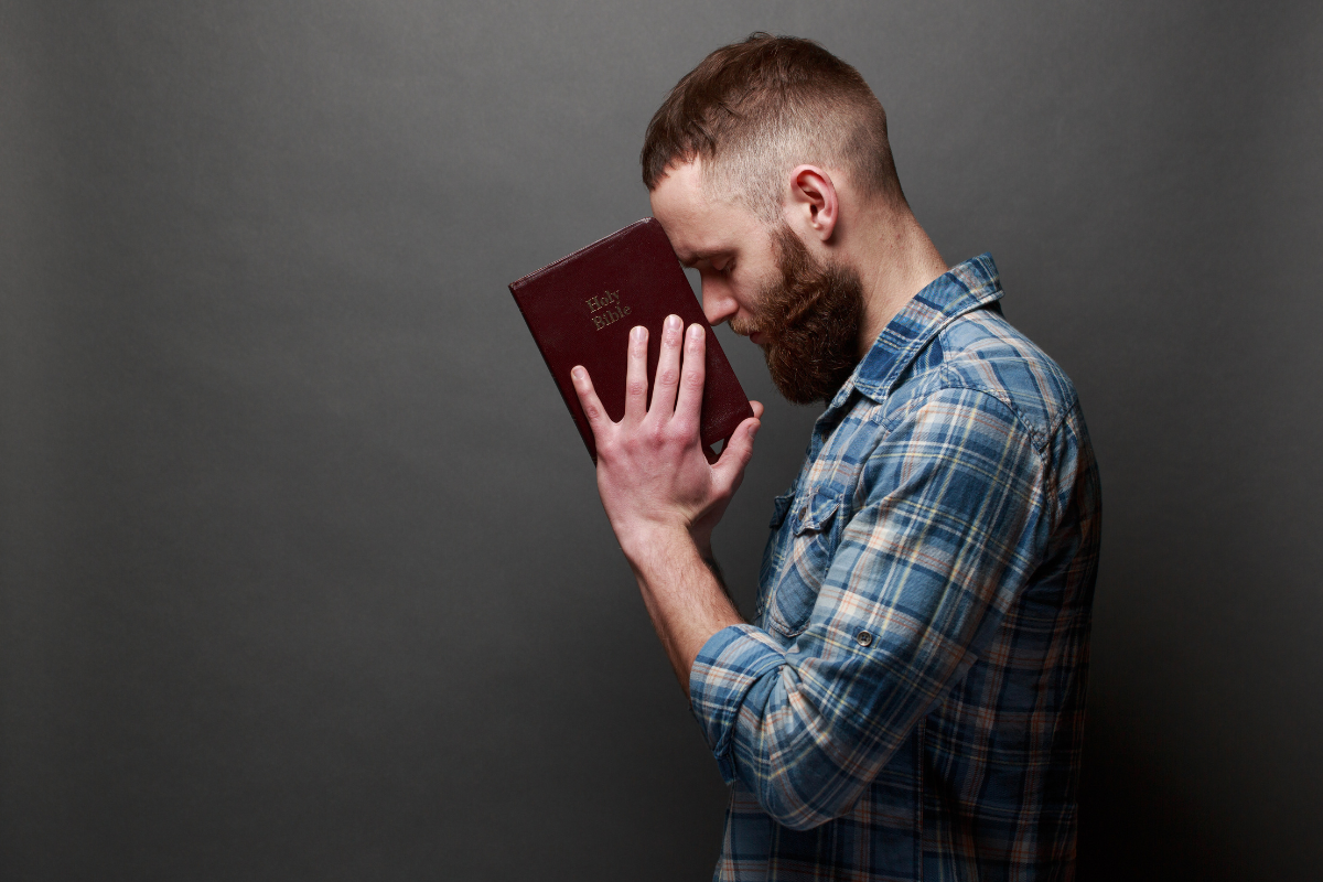 An image of a man holding a red Bible against his forehead.